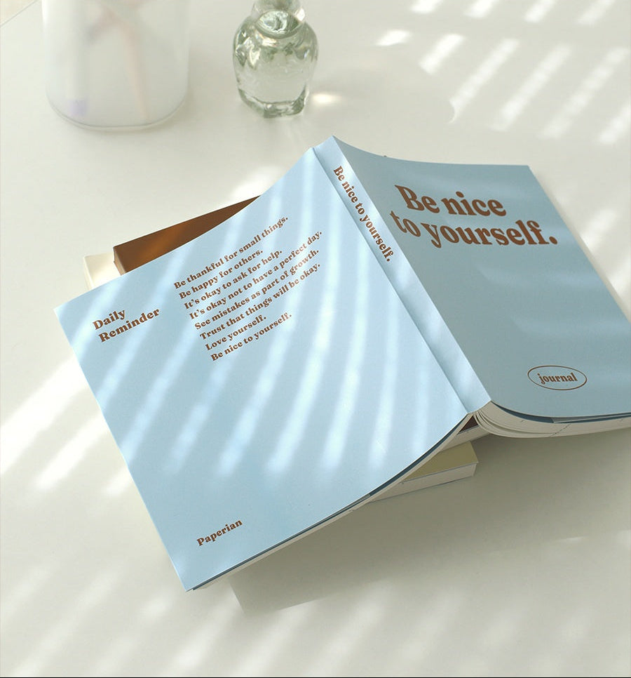 An open Korean journal from Paperian resting on a stack of notebooks in soft daylight, showing its cream interior pages