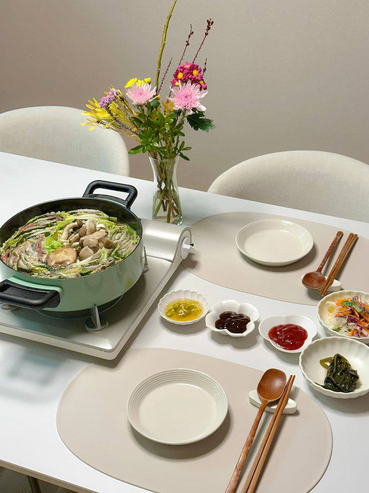 Dining table set with a hot pot, plates, and small dishes on a neutral background