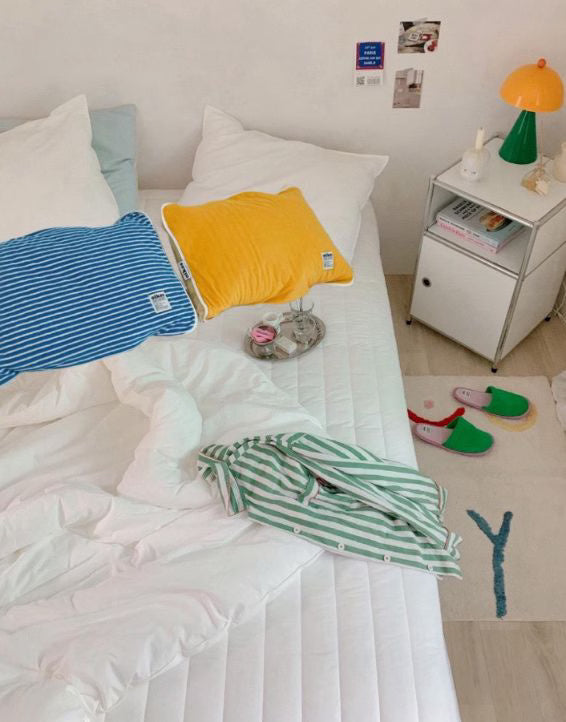 Bed with colorful pillows with colorful pillow covers from Oikos and a nightstand in a bedroom setting