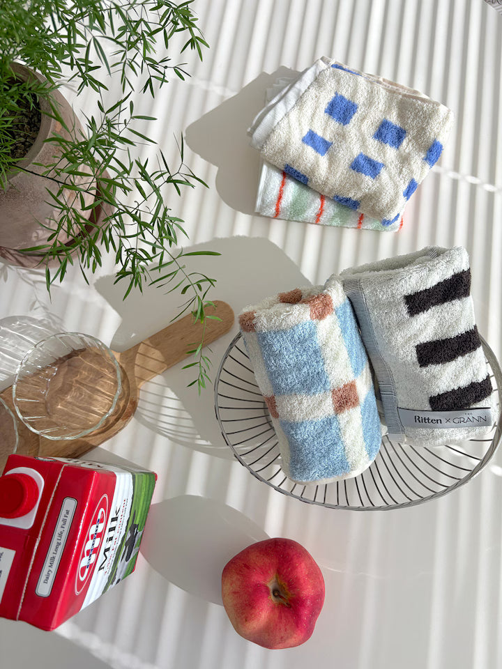 Colorful checkered towels on a wire rack with a plant, apple, and box in the background.